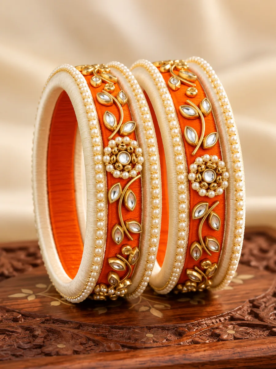 Orange & Ivory Pearl Kundan Designer Bangles — Elegant orange and ivory thread-wrapped bangles featuring pearl borders, gold-toned floral detailing, and sparkling Kundan-style stone accents.